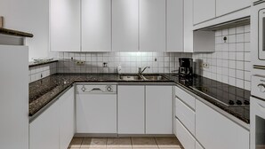 A modern kitchen with white cabinets, a black countertop, and a built-in dishwasher.