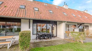A house with a tiled roof, large windows, and a patio with a table and chairs. - 3 bedroom accommodation in Nieuwpoort (Nieuwpoort)