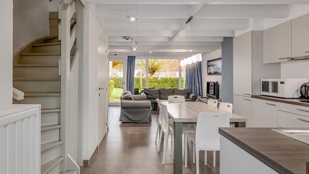 A modern kitchen with white cabinets, a dining area with a table and chairs, and a staircase leading to another level. - 3 bedroom accommodation in Nieuwpoort (Nieuwpoort)