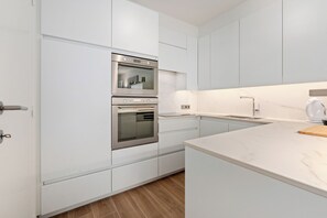 Una cocina moderna con armarios blancos, un horno doble, encimera de mármol y un lavamanos empotrado.