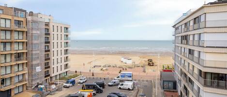 A coastal view with buildings, a beach, and parked vehicles.