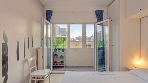 A bedroom with a bed, a chair, a shelf with potted plants, and a view of the city through a glass door. - 2 bedroom accommodation in Koksijde (Koksijde)