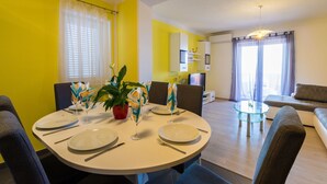 A dining area with a round table set for four, surrounded by chairs. There is a potted plant on the table, and the room has yellow walls. - Apartments Tomica (Novi Vinodolski)