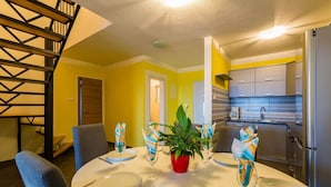 A dining area with a table set for four, a potted plant, and a kitchen visible in the background. - Apartments Tomica (Novi Vinodolski)