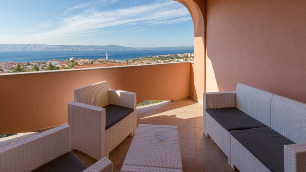 A balcony with wicker furniture, a view of the sea and distant buildings, and a clear sky. - Apartments Tomica (Novi Vinodolski)
