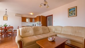 A modern living room with a beige sectional sofa, a wooden coffee table, and a dining area with wooden chairs and a red table. - Apartments Tomica (Novi Vinodolski)