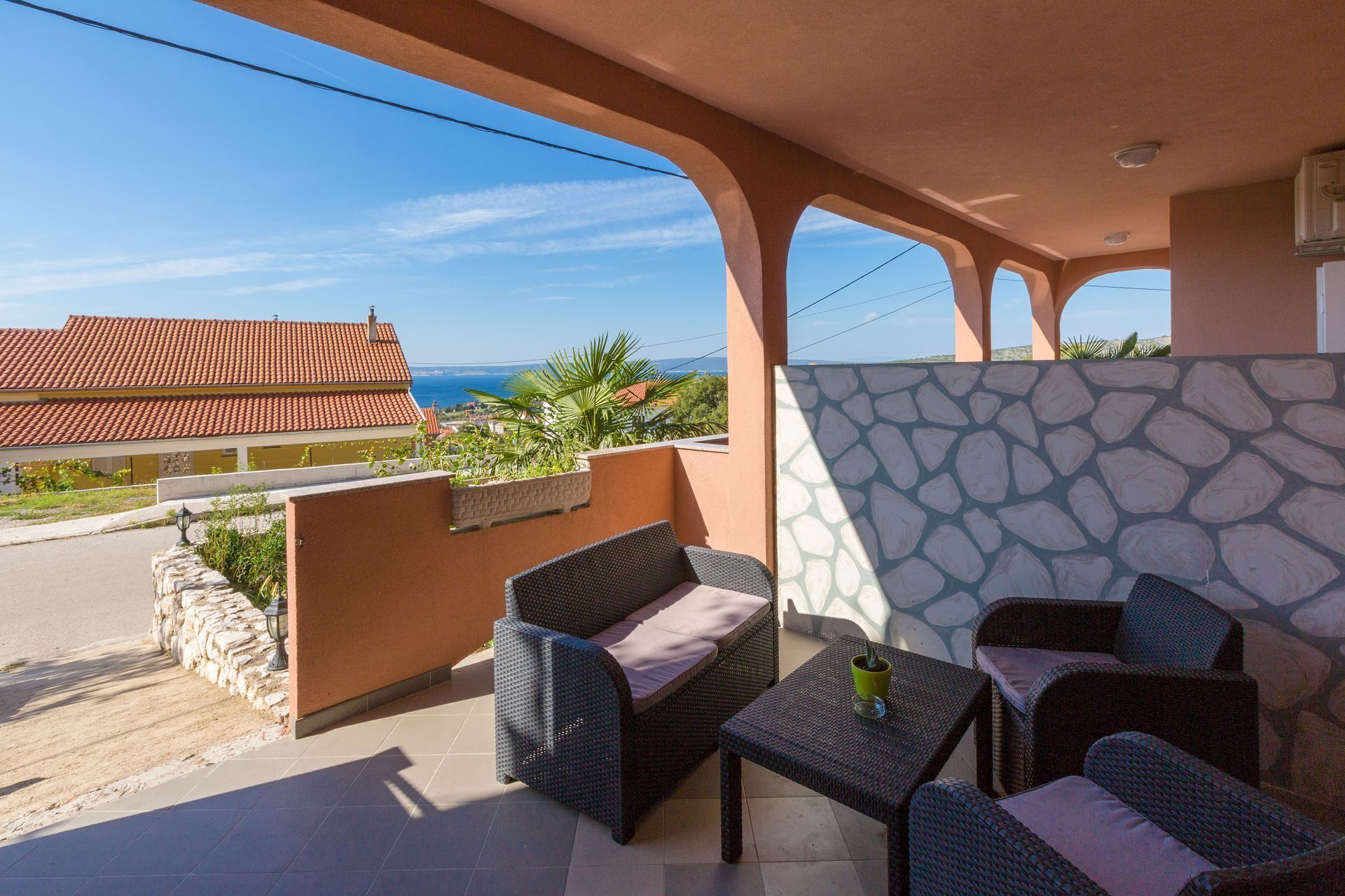 Ein Balkon mit Korbmöbeln, einer Steinmauer und Blick auf das Meer.