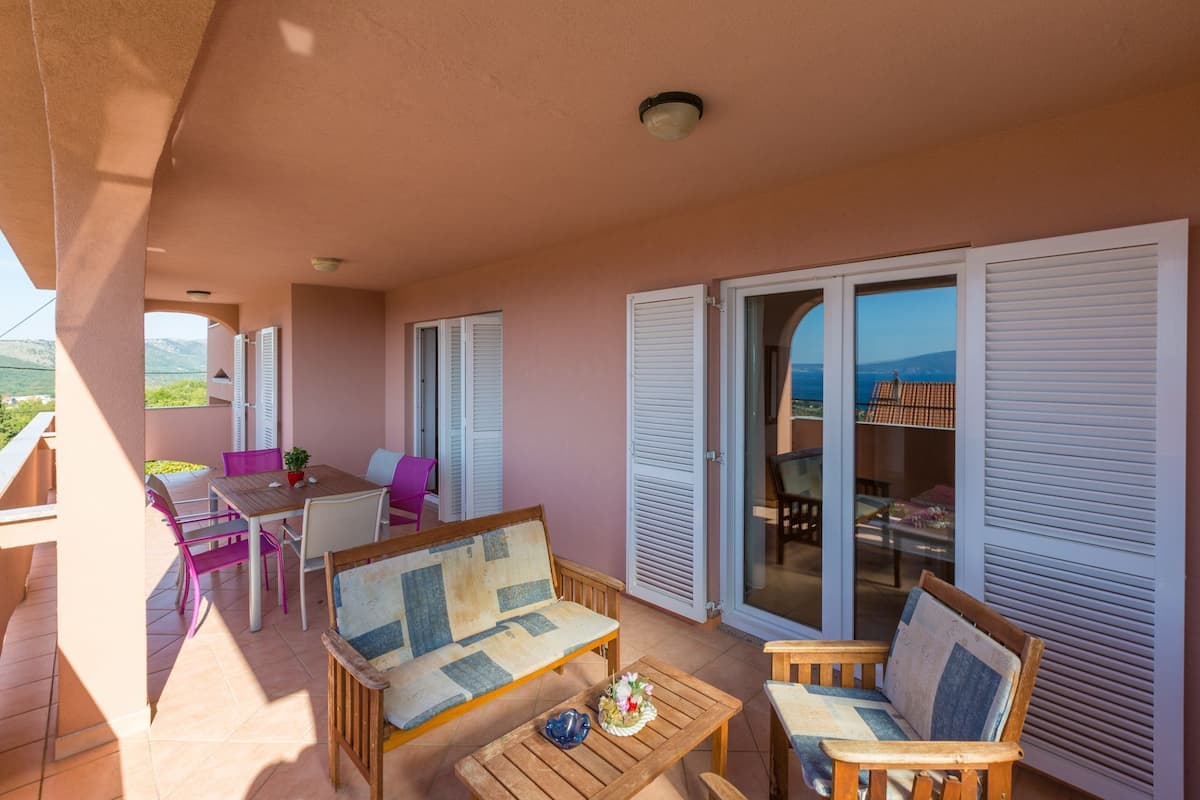 Ein Balkon mit Holztisch, zwei Stühlen, einer Couch und Meerblick.