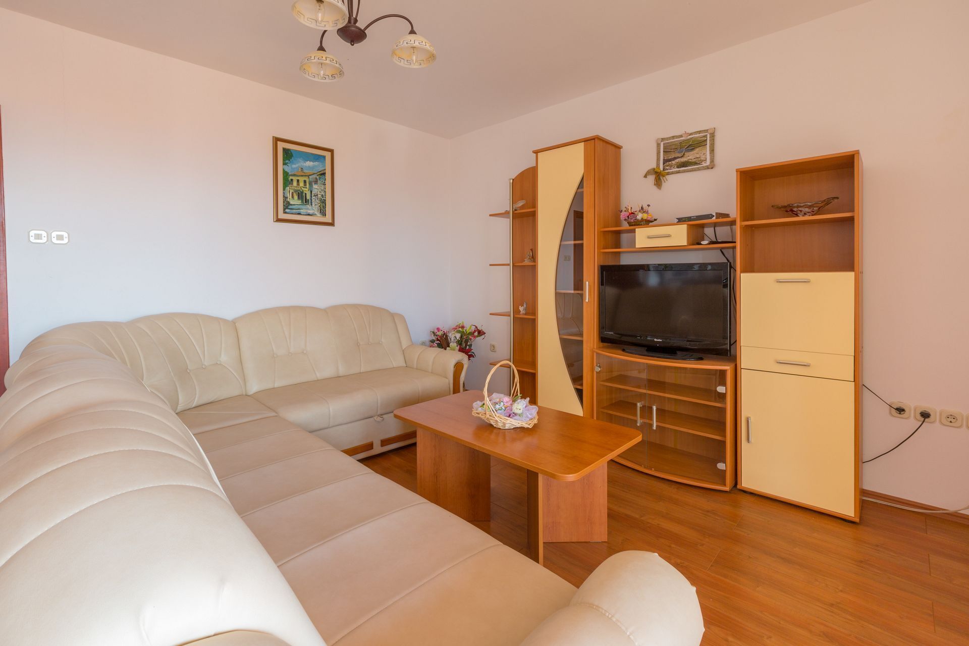 A living room with a sofa, TV, wooden cabinets, and a painting on the wall.