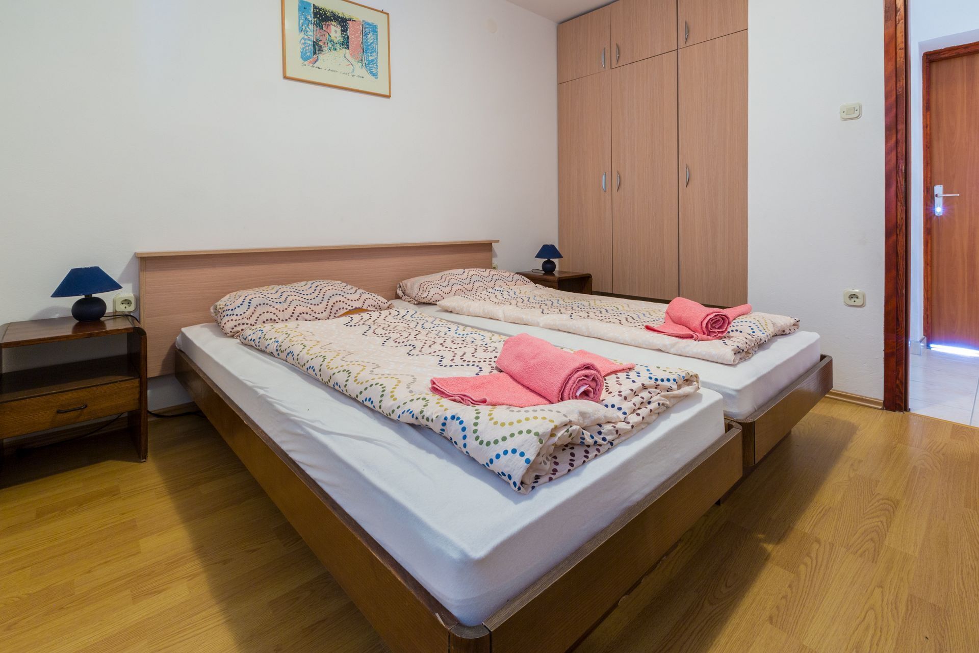A double bed with a polka dot duvet, a nightstand with a lamp, and a wooden wardrobe.