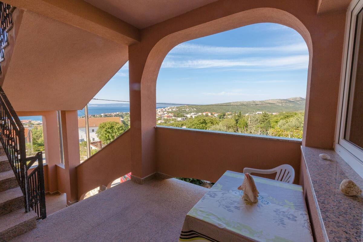 Ein Balkon mit Blick auf eine Küstenstadt, ein Tisch mit Tischdecke und ein Stuhl.