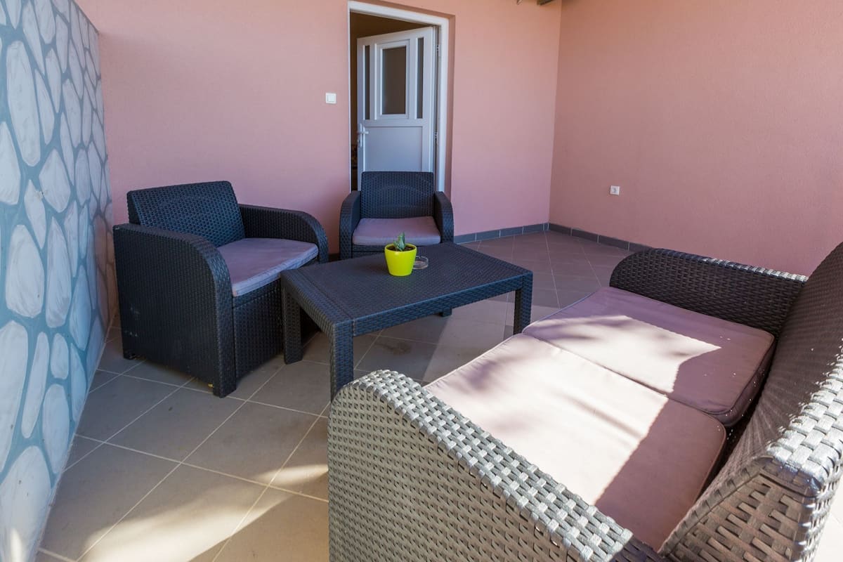 Eine Terrasse mit Korbmöbeln, darunter zwei Stühle, ein Sofa, ein kleiner Tisch und ein Blumentopf.