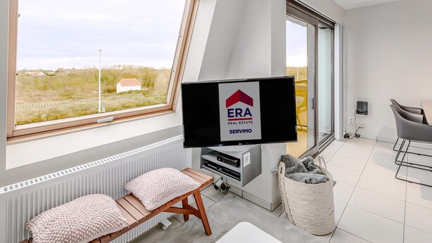 A modern hotel room with a large window, a flat-screen TV, a sofa, a chair, and a small table. - 2 bedroom accommodation in Oostduinkerke (Oostduinkerke)