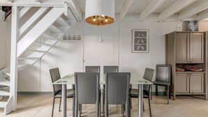 A dining area with a white staircase, a chandelier, and a cabinet with baskets.