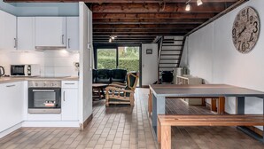 A kitchen with white cabinets, a microwave, and an oven. There is a wooden bench and a table with a clock on the wall.