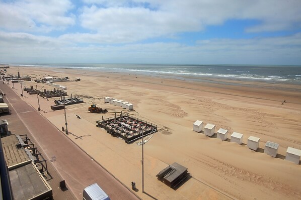 A beachside hotel with a long promenade, a parking area, and several beach huts.
