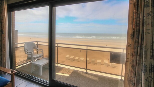Un balcon donnant sur la plage, une chaise en plastique blanche et une petite table.