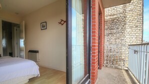 Une chambre à coucher avec un lit, une porte-fenêtre coulissante donnant sur un balcon avec un mur en briques et une rambarde en métal.