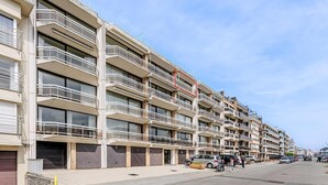 Ein mehrstöckiges Wohnhaus mit Balkonen, eine Straße davor und abgestellte Autos.
