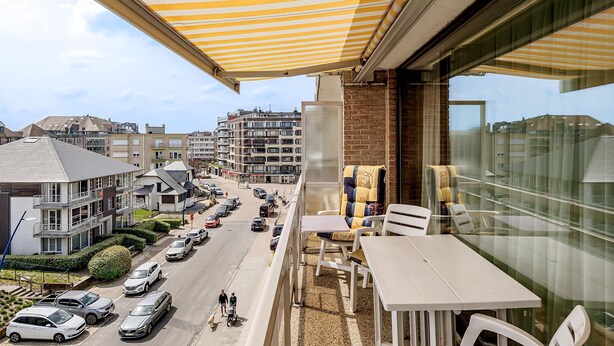 Ein Balkon mit gestreiftem Sonnenschirm, einem Tisch und Stühlen.