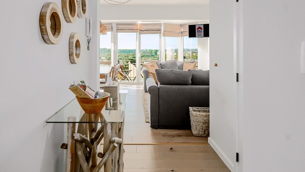 Un salon moderne avec un canapé gris, une table basse en verre et une vue sur un balcon aménagé avec du mobilier d’extérieur.