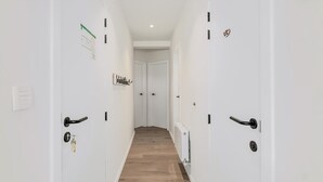 Un couloir étroit aux murs blancs et au plancher en bois, qui mène à une porte au fond.