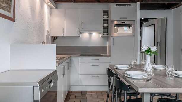 Una cocina moderna con armarios blancos, horno empotrado y comedor con una mesa de madera para cuatro personas.