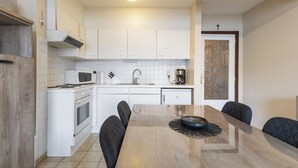 A modern kitchen with white cabinets, a microwave, stove, and a dining table with four chairs. - 2 bedroom accommodation in Koksijde (Koksijde)