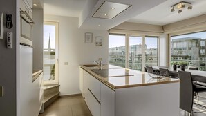 A modern kitchen with a large island, a dining area with a view, and a staircase leading to an upper level.