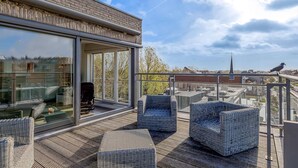 A modern outdoor deck with wicker furniture and a glass wall overlooking a cityscape.