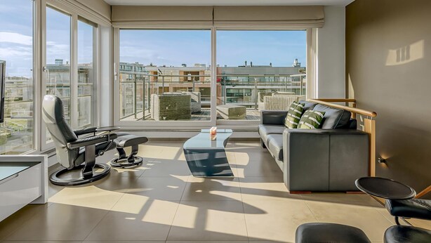 A modern living room with large windows, a sofa, a coffee table, and a chair.