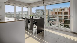 A modern kitchen with a dining area, large windows, and a view of the cityscape.