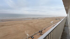 Vista da praia a partir de uma varanda com grade, praia arenosa e oceano ao fundo.