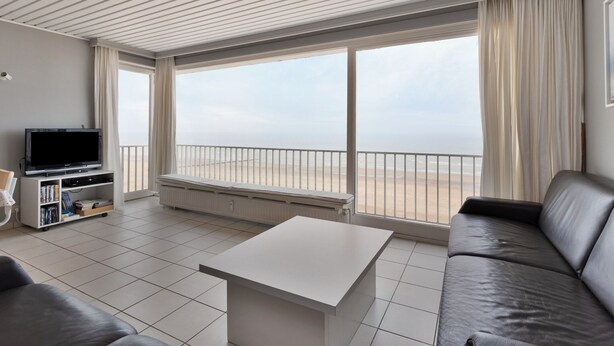 Uma sala de estar moderna com uma janela ampla, uma televisão de tela plana, um sofá e uma mesa de centro.