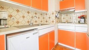 Eine Küche mit orangenen Schränken, einem weißen Kühlschrank und einer gemusterten Spritzschutzwand.