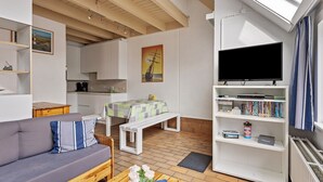 Ein kompakter Wohnraum mit Sofa, Esstisch, Bank, Fernseher und Bücherregal.