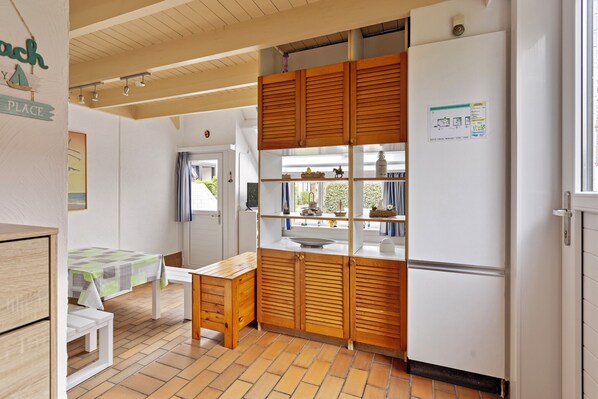 A compact kitchen with wooden cabinets, a refrigerator, and a dining area with a bench and table.