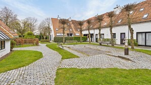 Ein Innenhof mit Kopfsteinpflasterwegen, einem weißen Gebäude mit Ziegeldach und einer Bank.