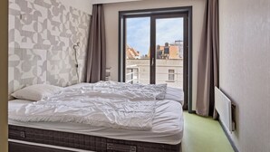 Una habitación de hotel con una cama grande, vistas a edificios a través de una ventana y un papel tapiz estampado.