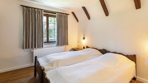 Un dormitorio con dos camas, una ventana con cortinas, una mesita de noche con lámpara y vigas de madera en la pared.