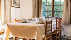 Mesa de comedor para cuatro personas con mantel blanco, sillas de madera y una ventana con cortinas.