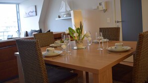Un coin repas avec une table en bois dressée pour quatre personnes, des chaises en osier et un vase rempli de fleurs.