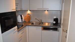 Une cuisine compacte avec des meubles blancs, un four encastré, une machine à café et une planche à découper en bois.