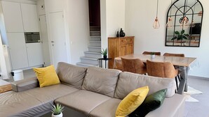 A modern living room with a beige sofa, a small black coffee table, and a dining area with a table and chairs. - 2 bedroom accommodation in Oostduinkerke (Oostduinkerke)