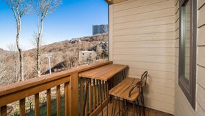 Una terraza de madera con una mesa y sillas, con vista a un paisaje montañoso con edificios.