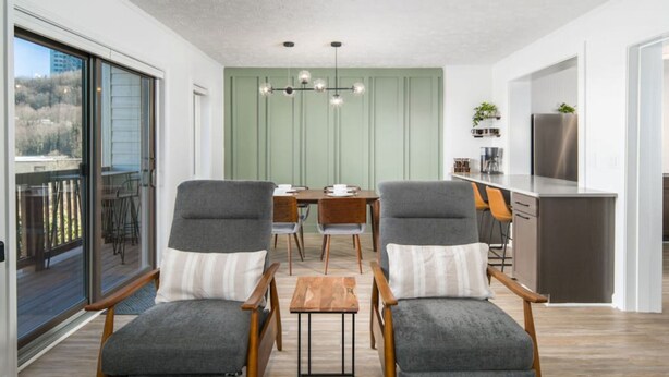 Cocina moderna con comedor, que presenta sillas tapizadas en gris, una mesa de madera y una pared de acento verde.