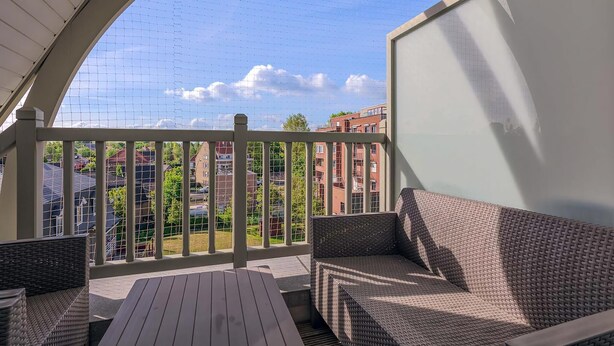 Ein überdachter Balkon mit Korbmöbeln, Blick auf Gebäude und einem klaren Himmel.