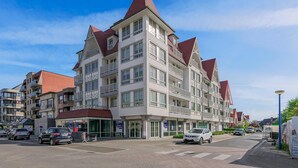 Ein mehrstöckiges Wohngebäude mit einer symmetrischen Fassade, großen Fenstern und einem markanten roten Dach.