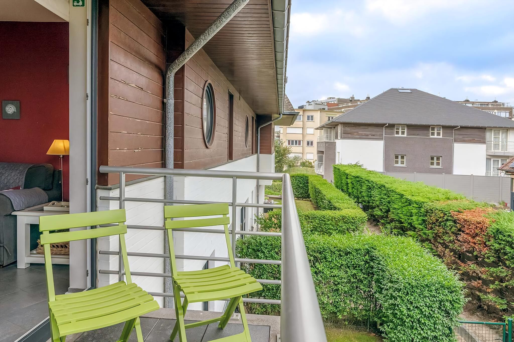 A balcony with green chairs, a table, and a lamp.