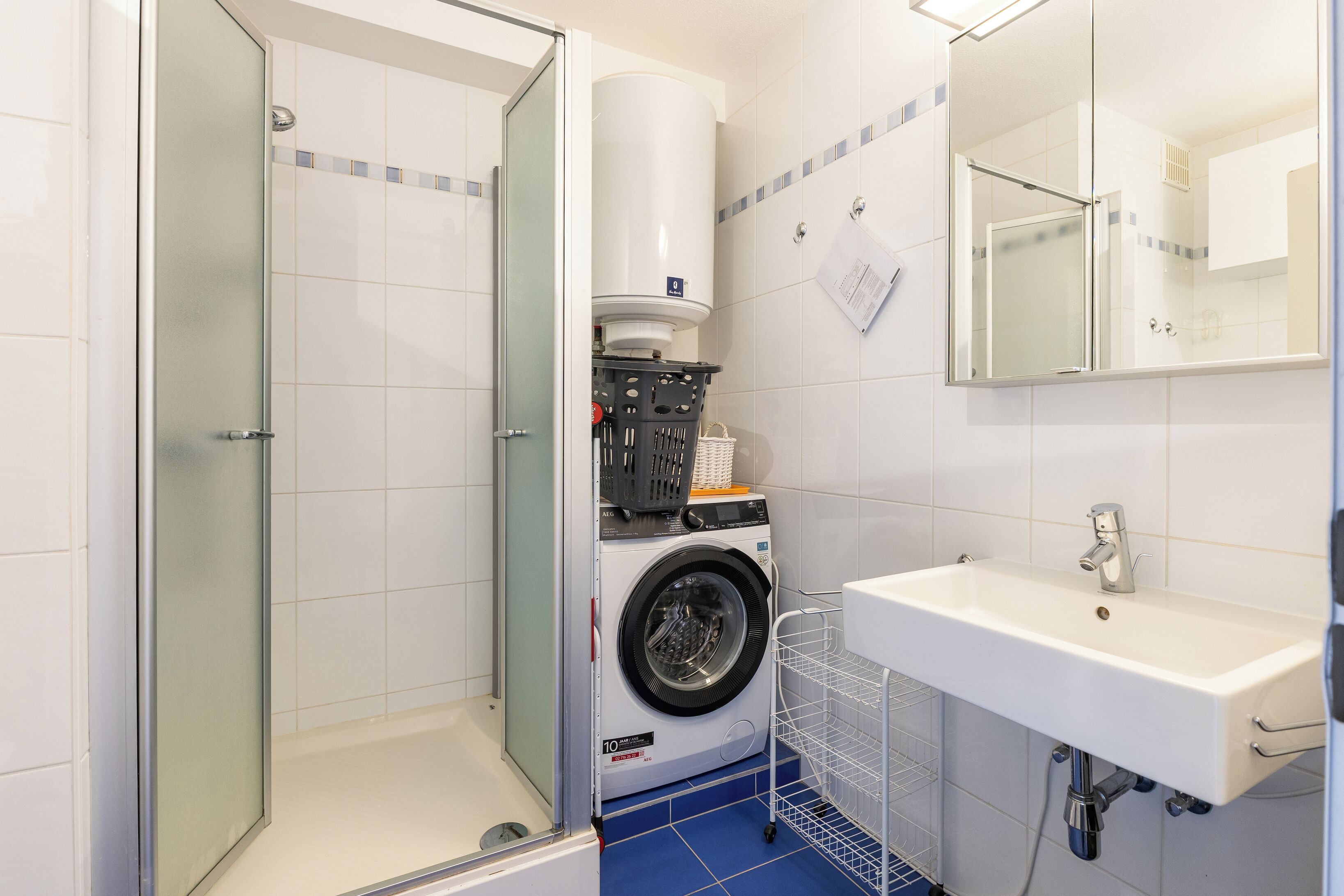 A compact bathroom with a glass shower enclosure, a front-loading washing machine, and a sink with a mirror.